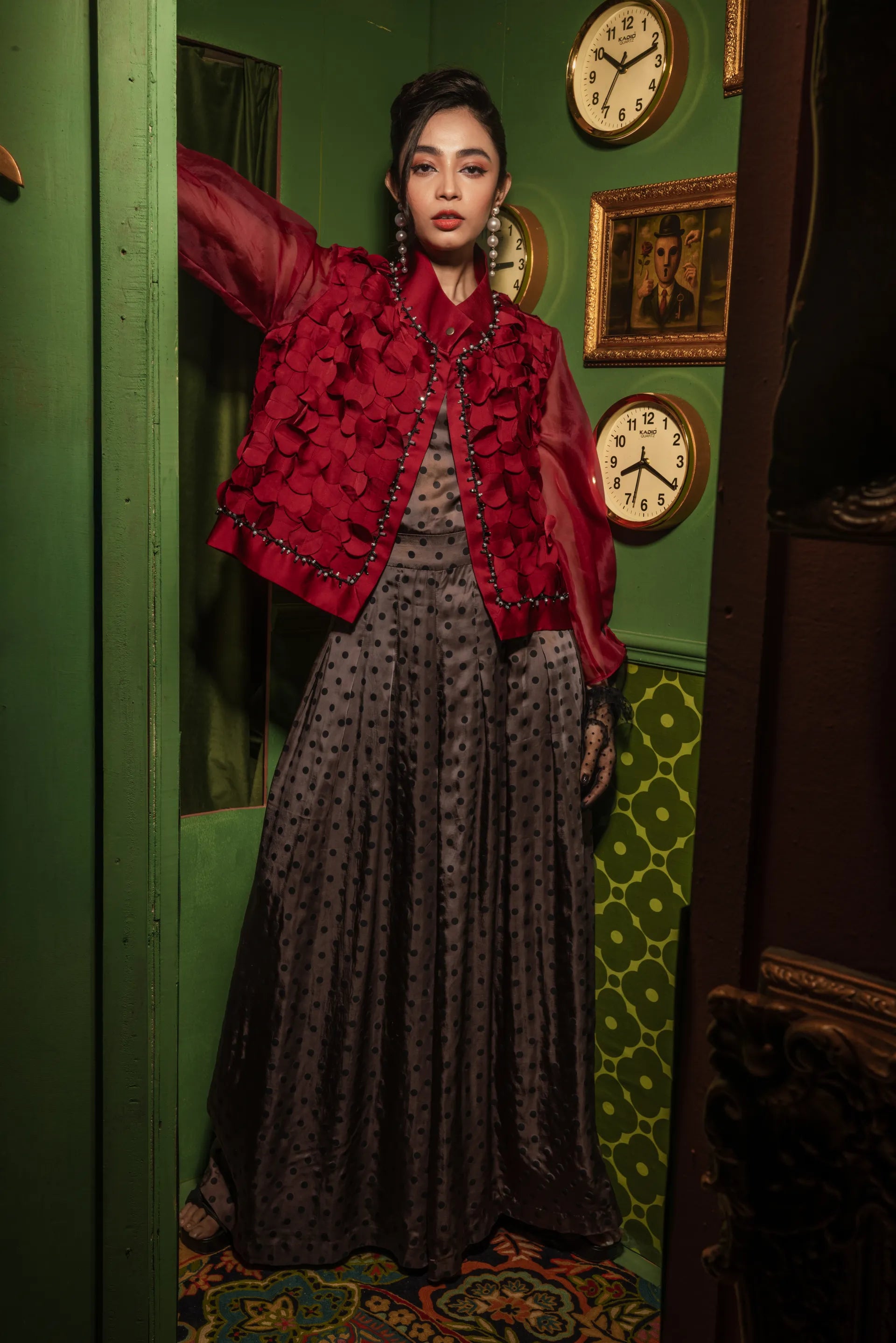 Woman in a red jacket and patterned dress standing in a room with green walls and decorative elements.
